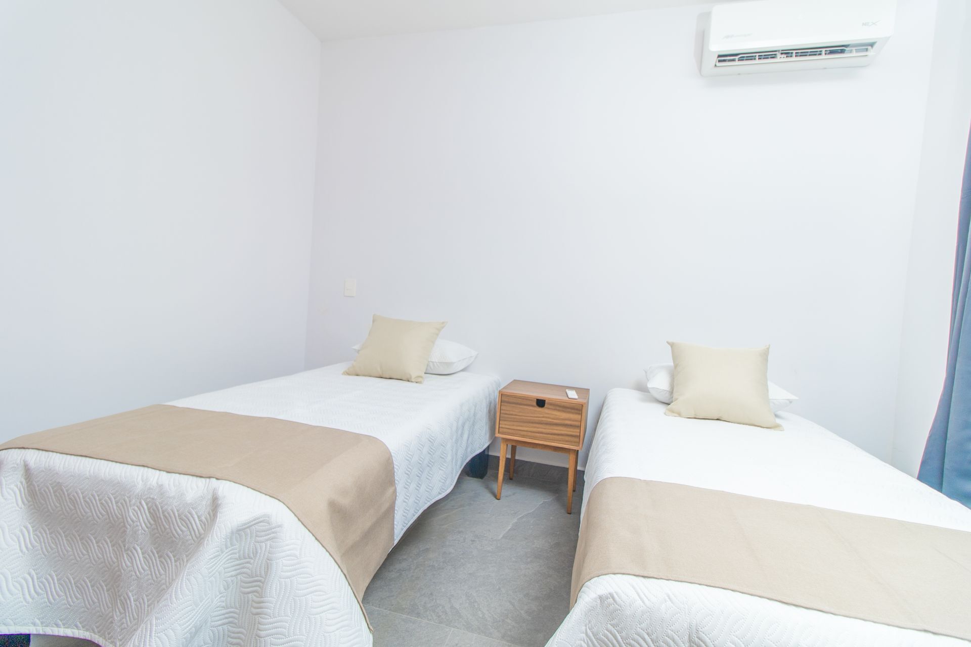 Une chambre double avec deux lits, une table de chevet en bois et un appareil de climatisation.