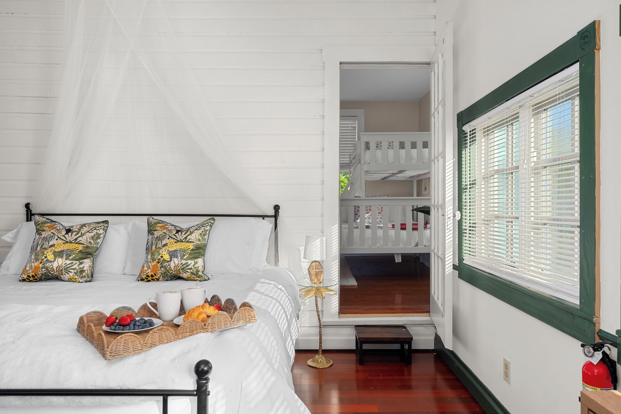 Una cama bien hecha con una bandeja de desayuno, una lámpara de noche y vistas a un balcón con barandilla.