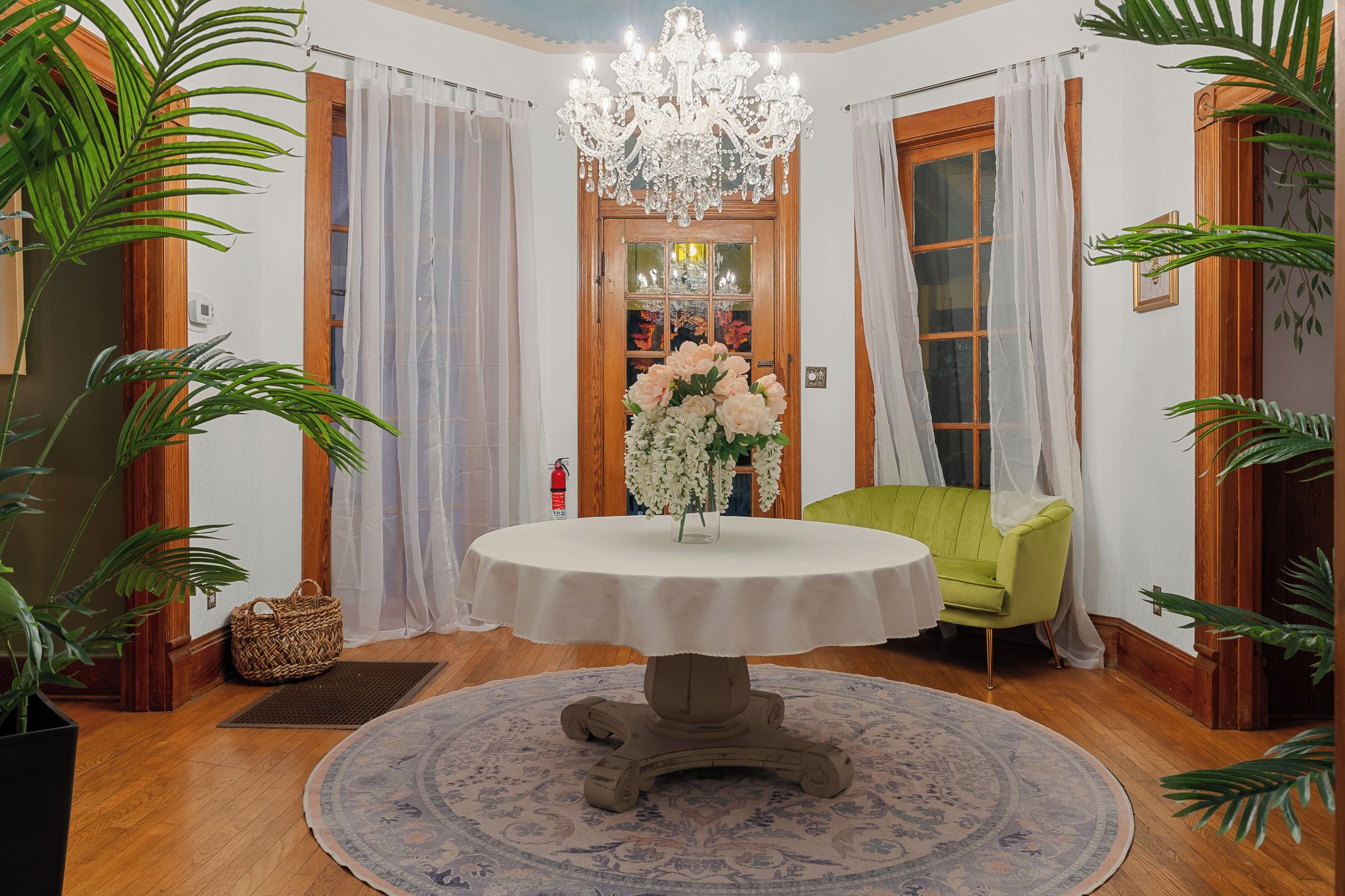 Une pièce avec une table ronde, un lustre, un fauteuil vert et un vase de fleurs.