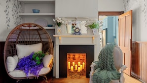 Een gezellige woonkamer met een open haard, een rieten stoel en een groene plaid.