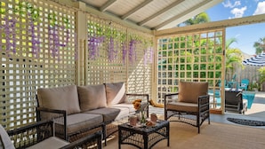 Een overdekt terras met rieten meubels, een comfortabele bank en een tafel met decoratieve objecten.