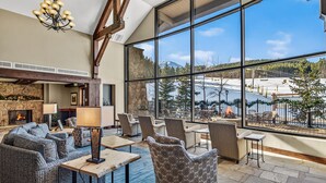 A spacious lounge with large windows, a stone fireplace, and comfortable seating.