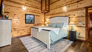 A wooden-paneled bedroom with a bed, a nightstand, a lamp, and a framed picture on the wall. - Pvt Indoor Pool, Gorgeous 6-BR Cabin, Theater, BBQ (Sevierville)