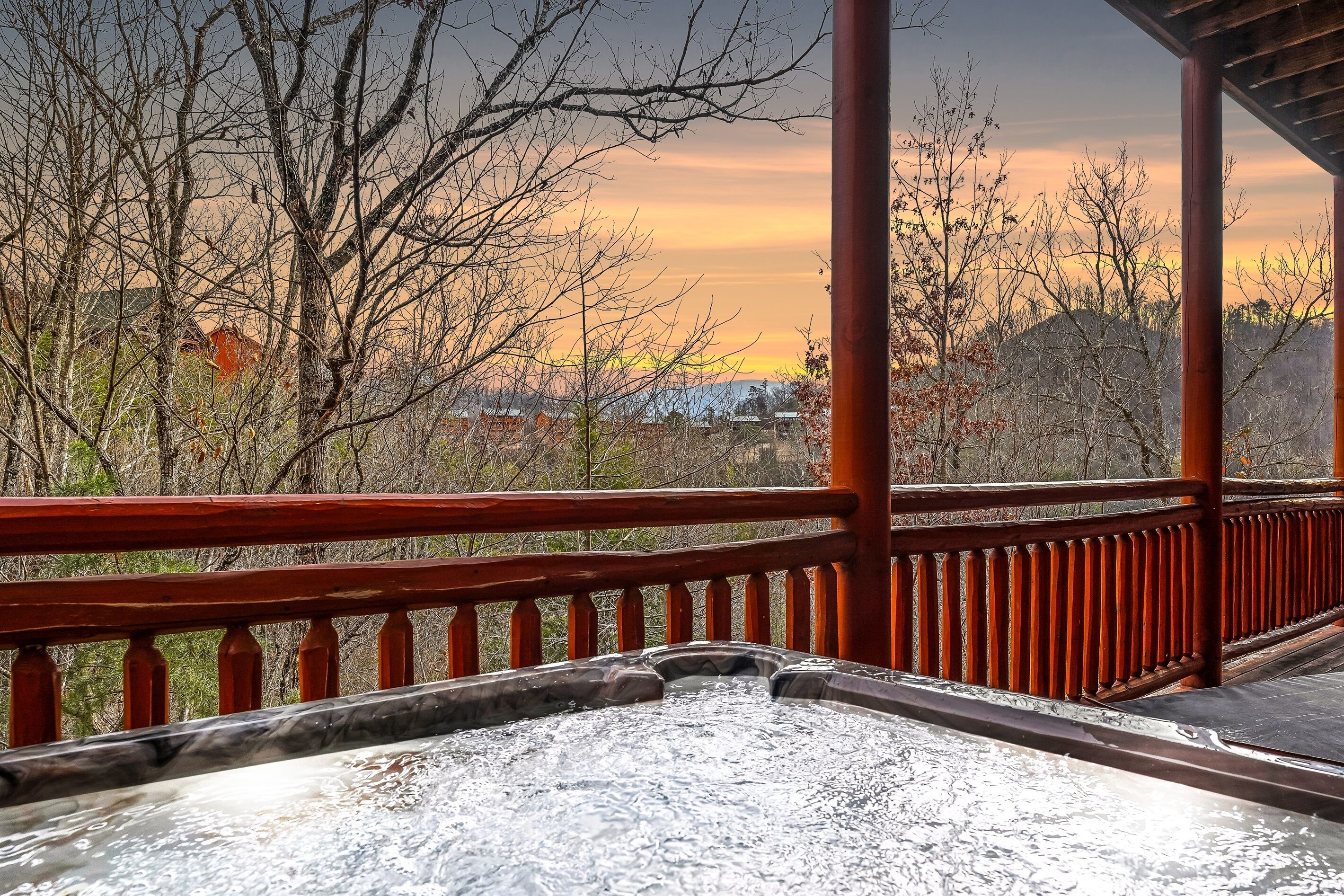A hot tub with a wooden railing and a view of trees and buildings in the background.