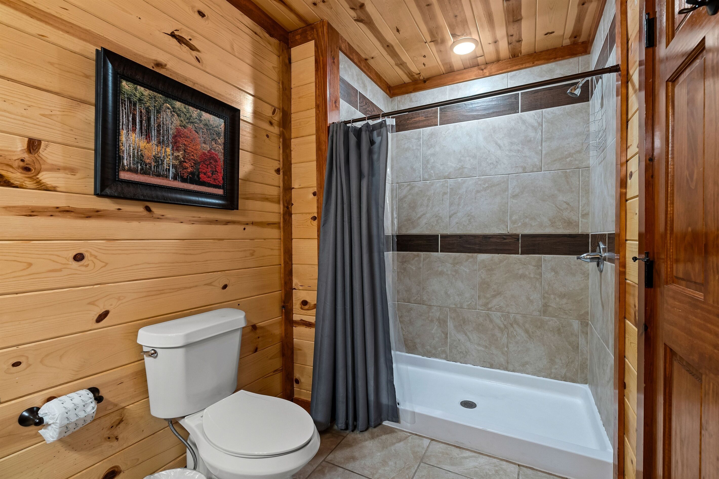 A wooden-paneled bathroom with a toilet, a shower with a curtain, and a framed picture on the wall.