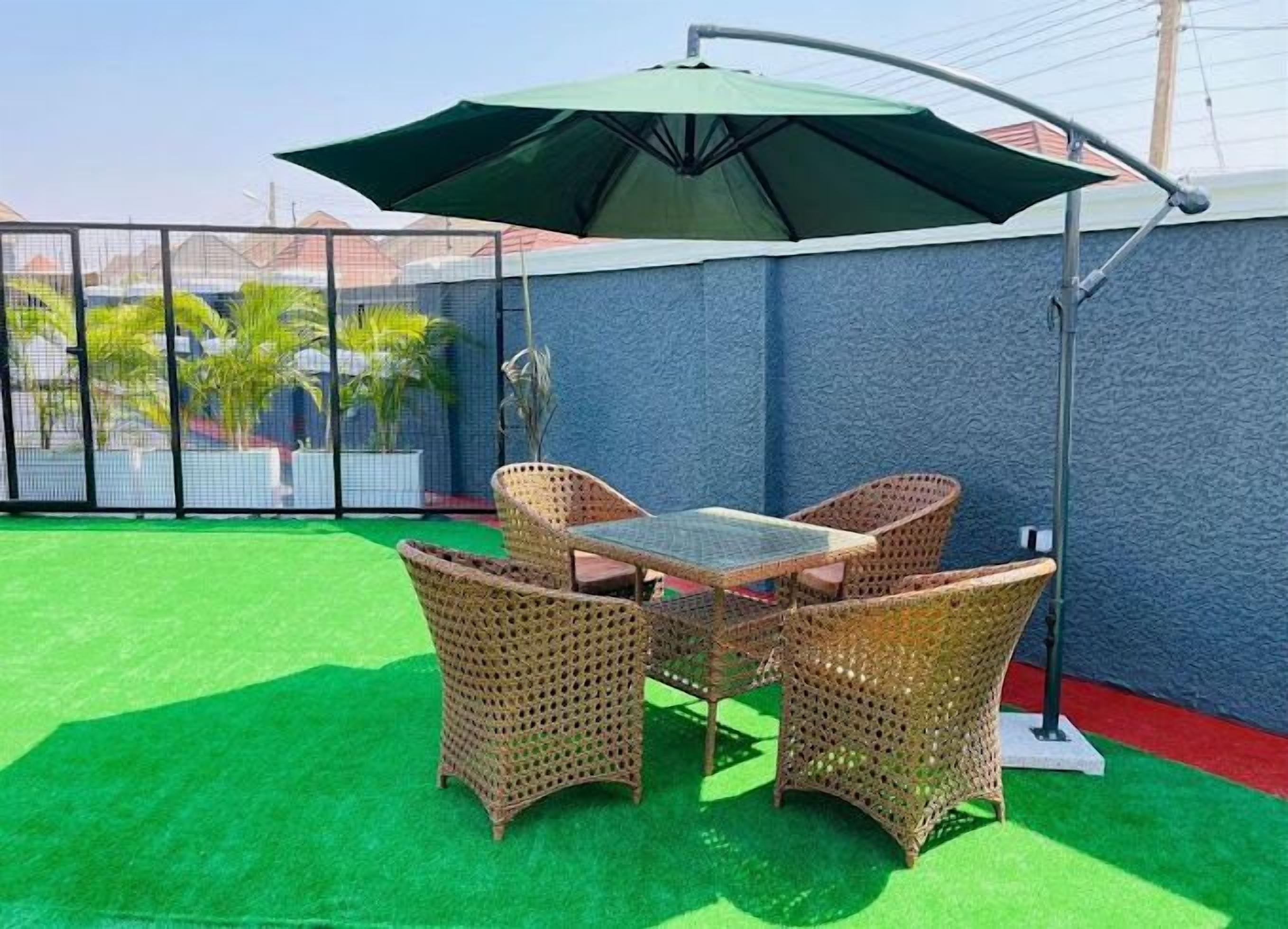 A patio with a table and chairs, an umbrella, and a green artificial turf.