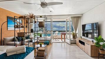 Ein modernes Wohnzimmer mit großem Fernseher, Deckenventilator, Sofa, Couchtisch und Blick ins Freie.