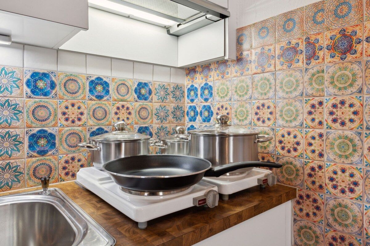 Een keuken met kleurrijke tegels, een fornuis, pannen en een spoelbak.