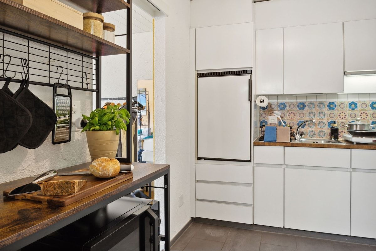 A kitchen with white cabinets, a refrigerator, a wooden countertop, and a potted plant.