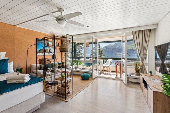 A modern living room with a sofa, a coffee table, and a bookshelf. There is a large window with a view of the outdoors.