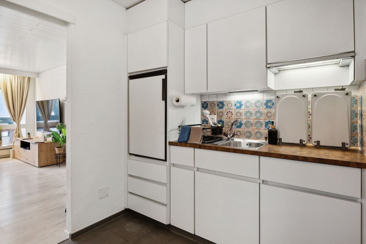 A modern kitchen with white cabinetry, a wooden countertop, a built-in oven, and a tiled backsplash.
