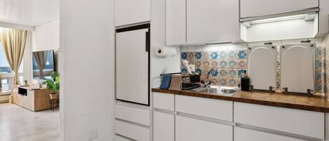 A modern kitchen with white cabinetry, a wooden countertop, a built-in oven, and a tiled backsplash.