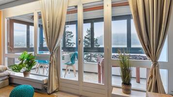 Ein Zimmer mit einer Schiebetür zum Balkon, einem Sofa, einem Türkis-Hocker und Topfpflanzen.