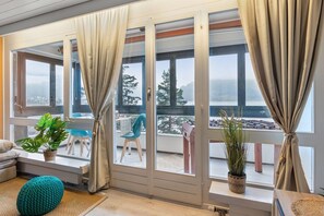 A room with a sliding glass door leading to a balcony, a sofa, a teal pouf, and potted plants.