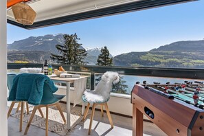 Ein Balkon mit einer Tischkicker-Anlage, einem Tisch mit Flaschen und Snacks sowie Bergblick.