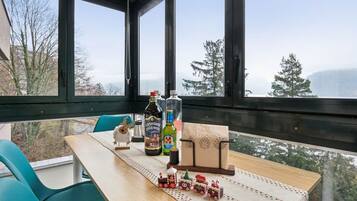 Ein Zimmer mit gedecktem Tisch für zwei Personen, einem kleinen Spielzug und Blick auf Bäume und Berge durch große Fenster.
