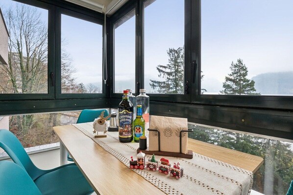 A room with a table set for two, a small toy train, and a view of trees and mountains through large windows.