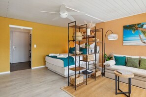 A room with a bed, a sofa, a standing shelf unit, and a ceiling fan.
