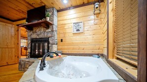 Un baño con lavamanos de piedra, una bañera con burbujas, una chimenea de piedra y un cartel que dice 'Don't Wake the Bear'.