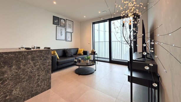 Een moderne woonkamer met een marmeren aanrecht, een zwarte bank met gele kussens, een ronde salontafel en een decoratieve tak met verlichting.