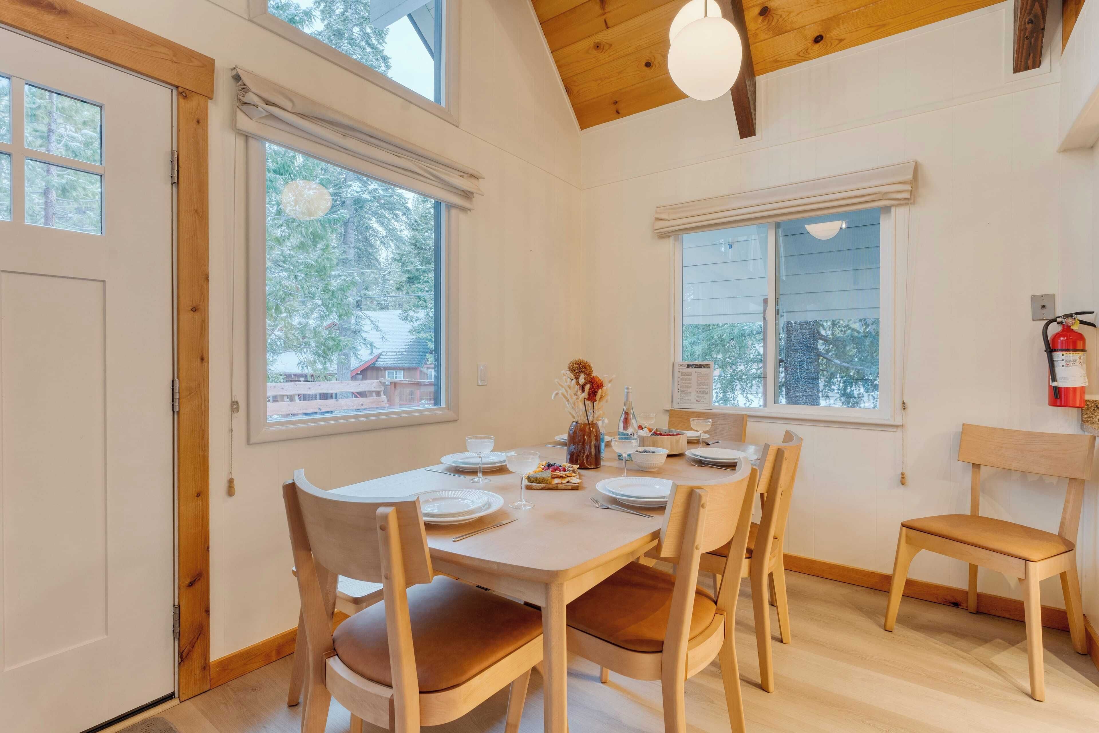 Un espace repas comprenant une table et des chaises en bois, de grandes fenêtres et un luminaire au plafond.