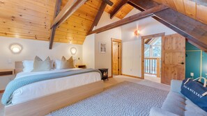 A bedroom with a bed, a nightstand, a wall-mounted light, a wooden door, and a view of the outdoors. - Peaceful Tahoe Retreat by Avantstay Cozy Modern Cabin Sauna, Hot Tub + Fireplace Near Lake (Carnelian Bay)