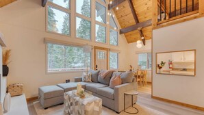 A spacious living room with a large window, a grey sofa, a coffee table, and a wooden ceiling. - Peaceful Tahoe Retreat by Avantstay Cozy Modern Cabin Sauna, Hot Tub + Fireplace Near Lake (Carnelian Bay)