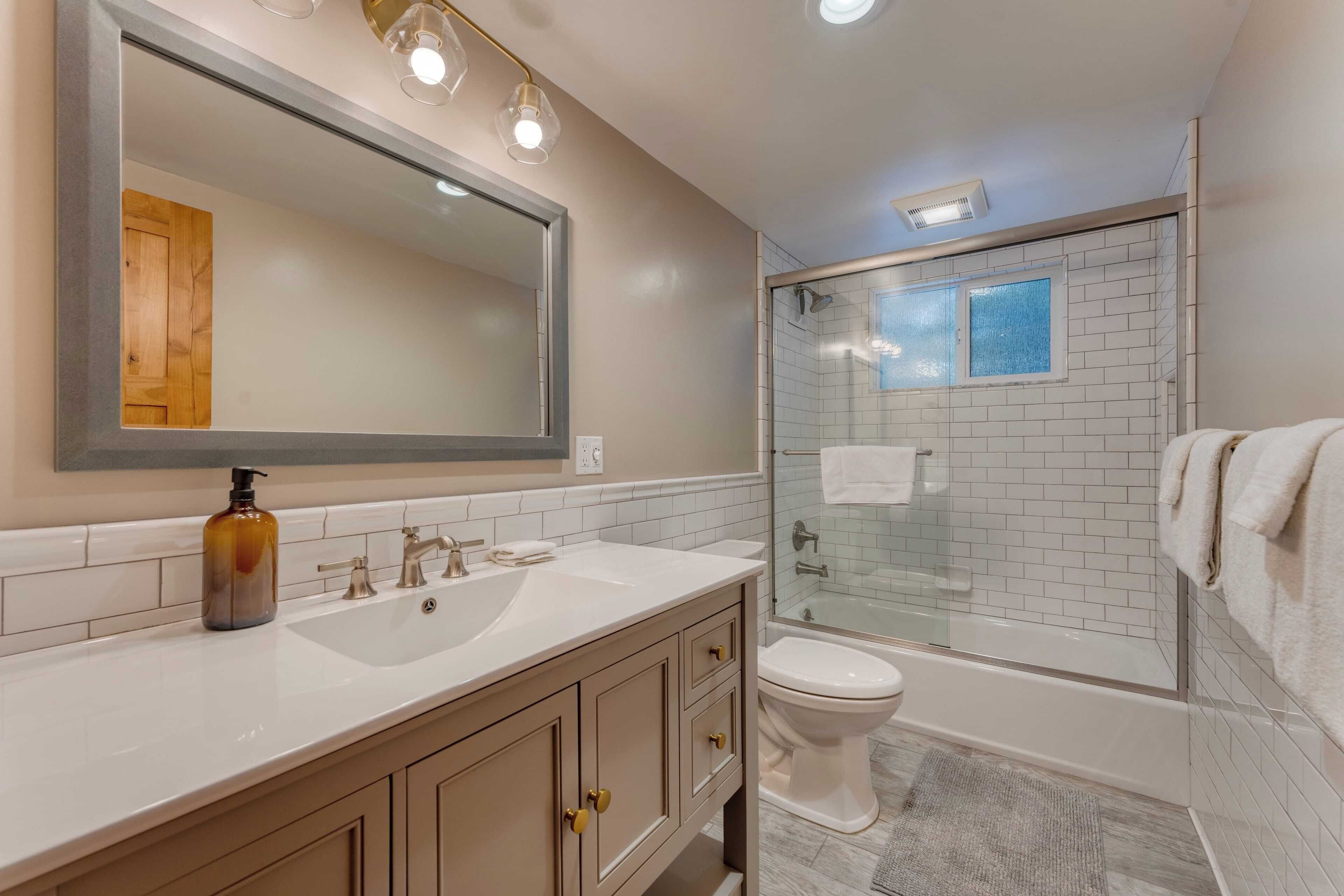 A bathroom with a large mirror, a sink, a toilet, and a glass-enclosed shower area.