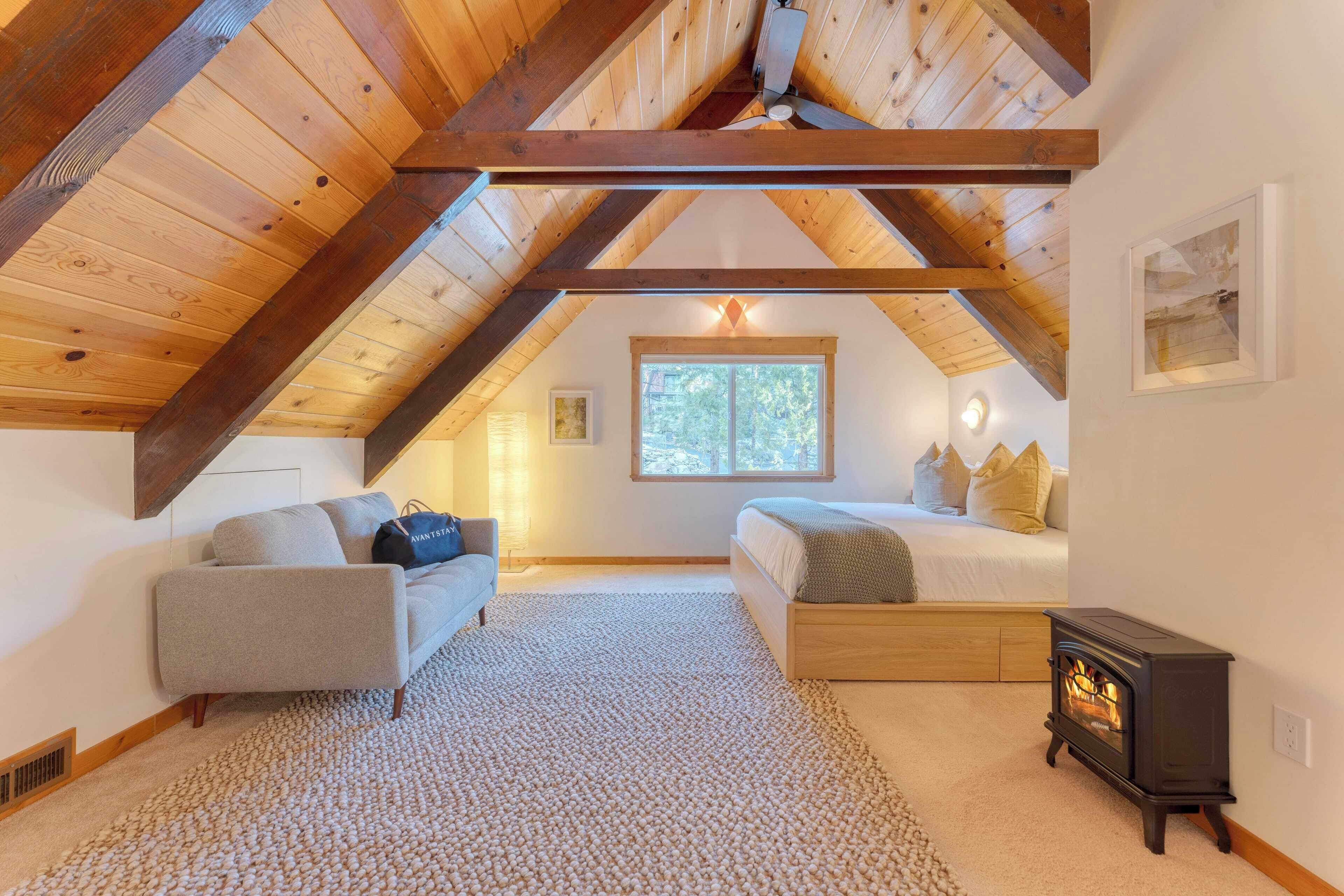 A cozy attic bedroom with a sloped ceiling, a bed, a sofa, a fireplace, and a window providing natural light.