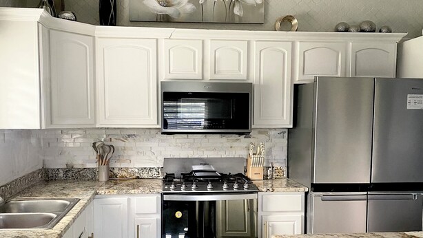 A modern kitchen with white cabinetry, stainless steel appliances, granite countertops, and a decorative chandelier. - Keepsake Oasis, Mid-Island 3-Bed Modern Cozy Home with AC, WiFi, Quiet Residence (Christiansted)