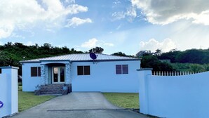 A single-story house with a concrete driveway leading to a gated entrance. - Keepsake Oasis, Mid-Island 3-Bed Modern Cozy Home with AC, WiFi, Quiet Residence (Christiansted)