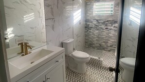 A modern bathroom with a marble vanity, a toilet, and a shower area with patterned tiles. - Keepsake Oasis, Mid-Island 3-Bed Modern Cozy Home with AC, WiFi, Quiet Residence (Christiansted)
