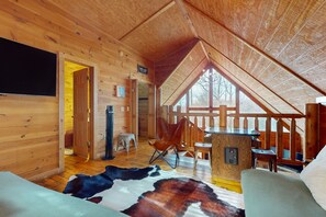 Cozy cabin-style room with a high ceiling, plush sofa, and wooden dining table.