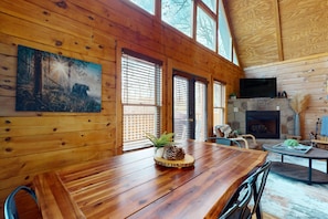 Cozy cabin interior with a large dining table, stone fireplace, and comfortable seating area.