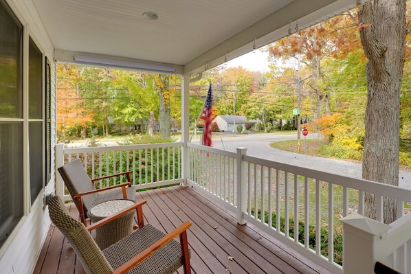 Een houten veranda met rieten stoelen en een vlag.
