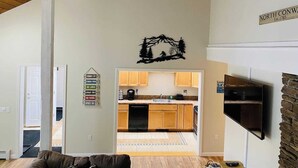 A living room with a stone fireplace, a TV mounted on the wall, and a kitchen visible through an open door. - Charming 2-bedroom house with AC, WiFi in North Conway (North Conway)