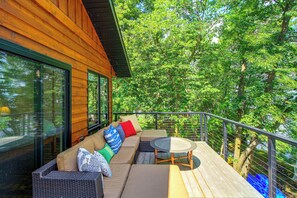 A wooden deck with a sofa and a round table, overlooking a dense forest. - Short Drive to Itasca State Park - Waterfront Home (Park Rapids)