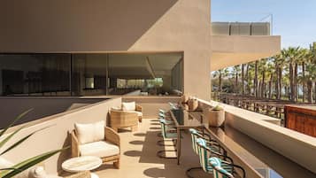 Un área de estar moderna al aire libre con mobiliario de mimbre y sillas a rayas, con vistas a una piscina y palmeras.