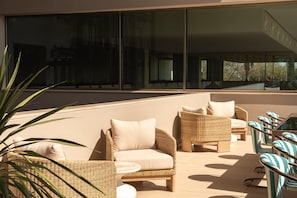 A modern outdoor seating area with wicker furniture and a glass table, overlooking a building. - Kimpton Atlantico Algarve (Albufeira)