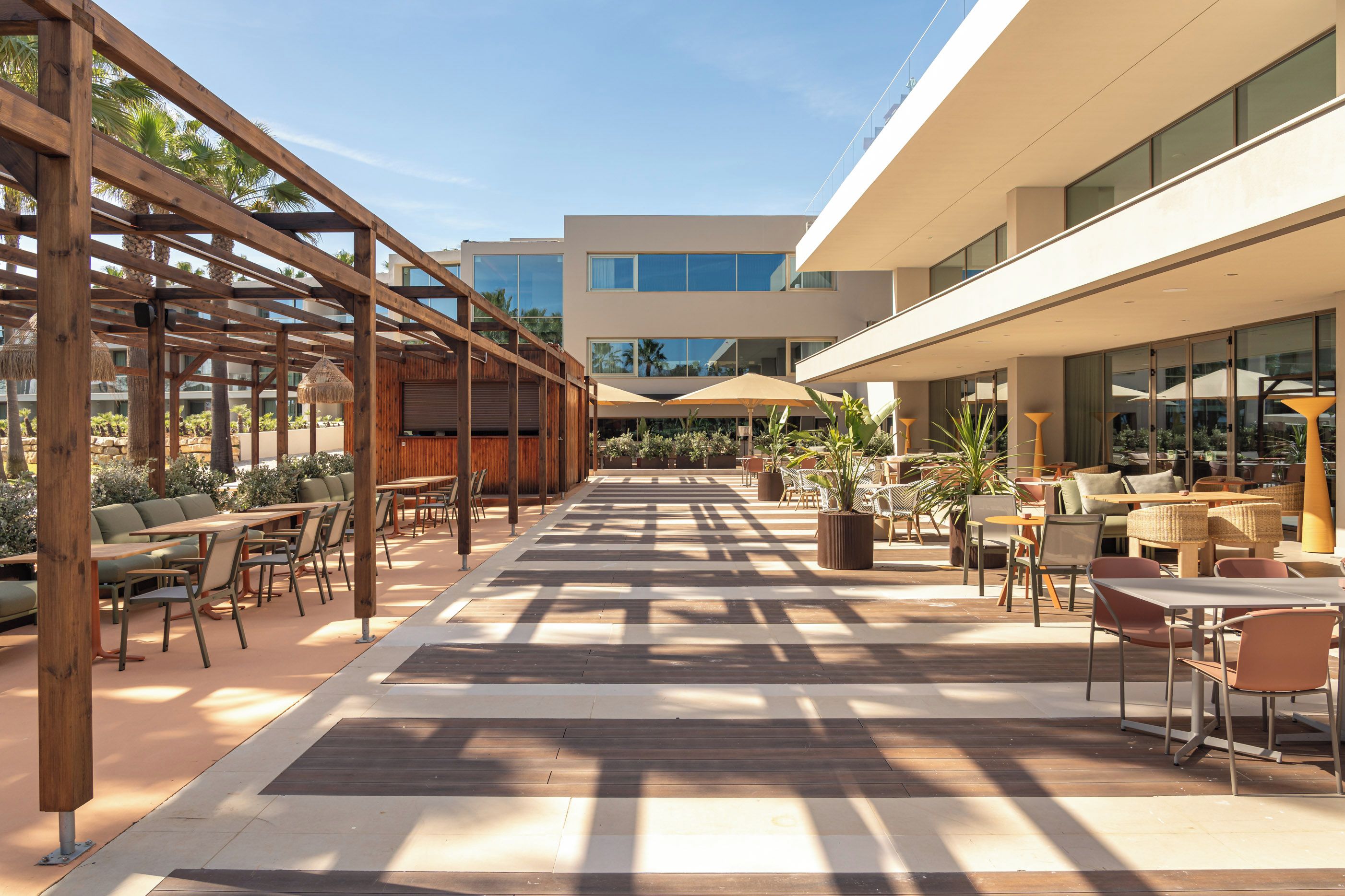 Een terras buiten met houten pergola’s, zitplekken en parasols.