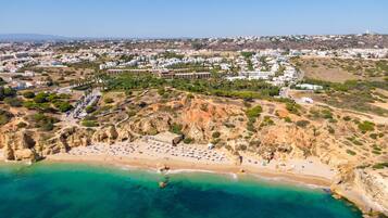 Una vista aèria d'una població costanera amb una platja, edificis i un paisatge amb turons.