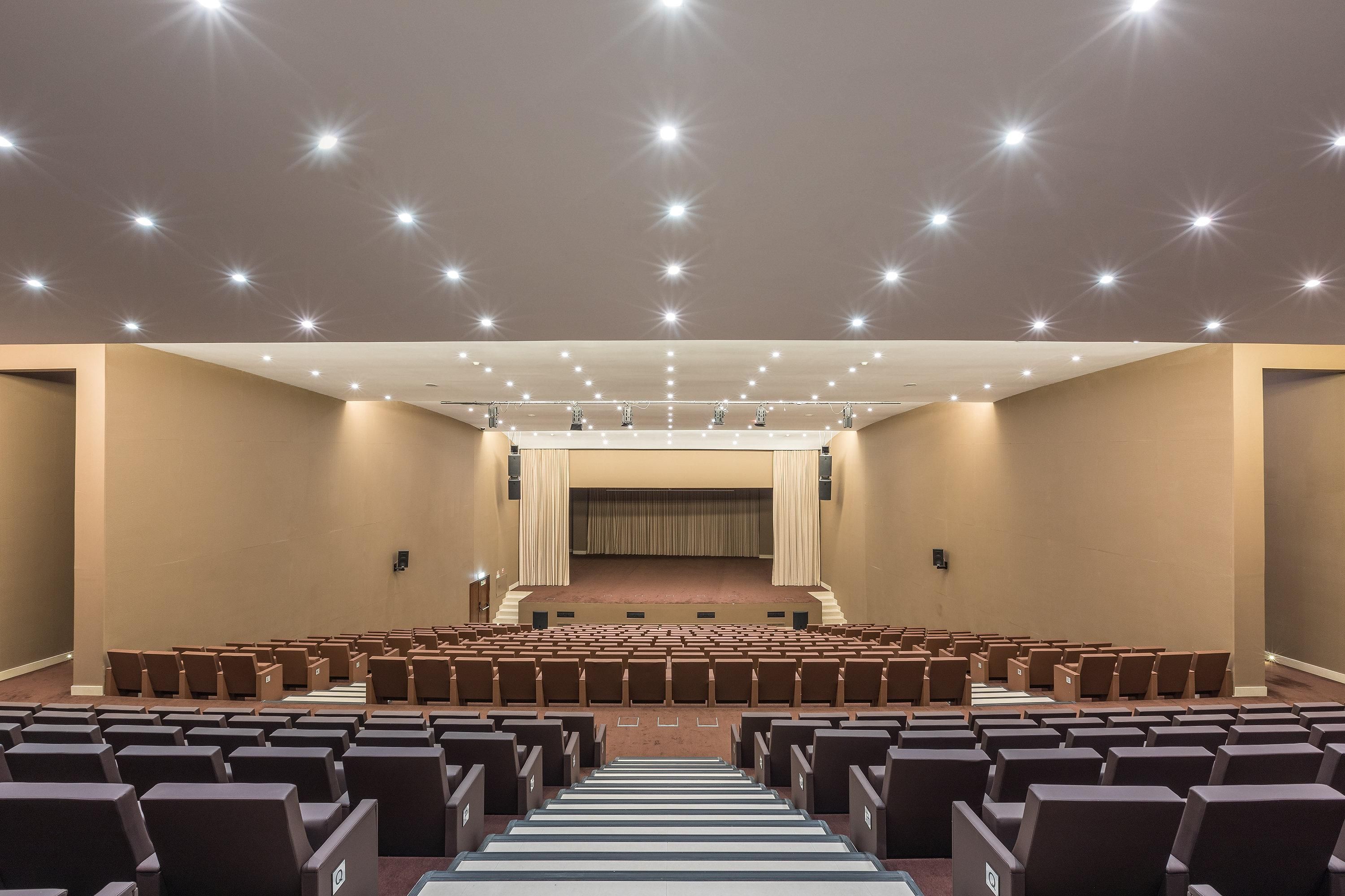 Un gran auditorio con filas de asientos, un escenario y un techo con múltiples luces.