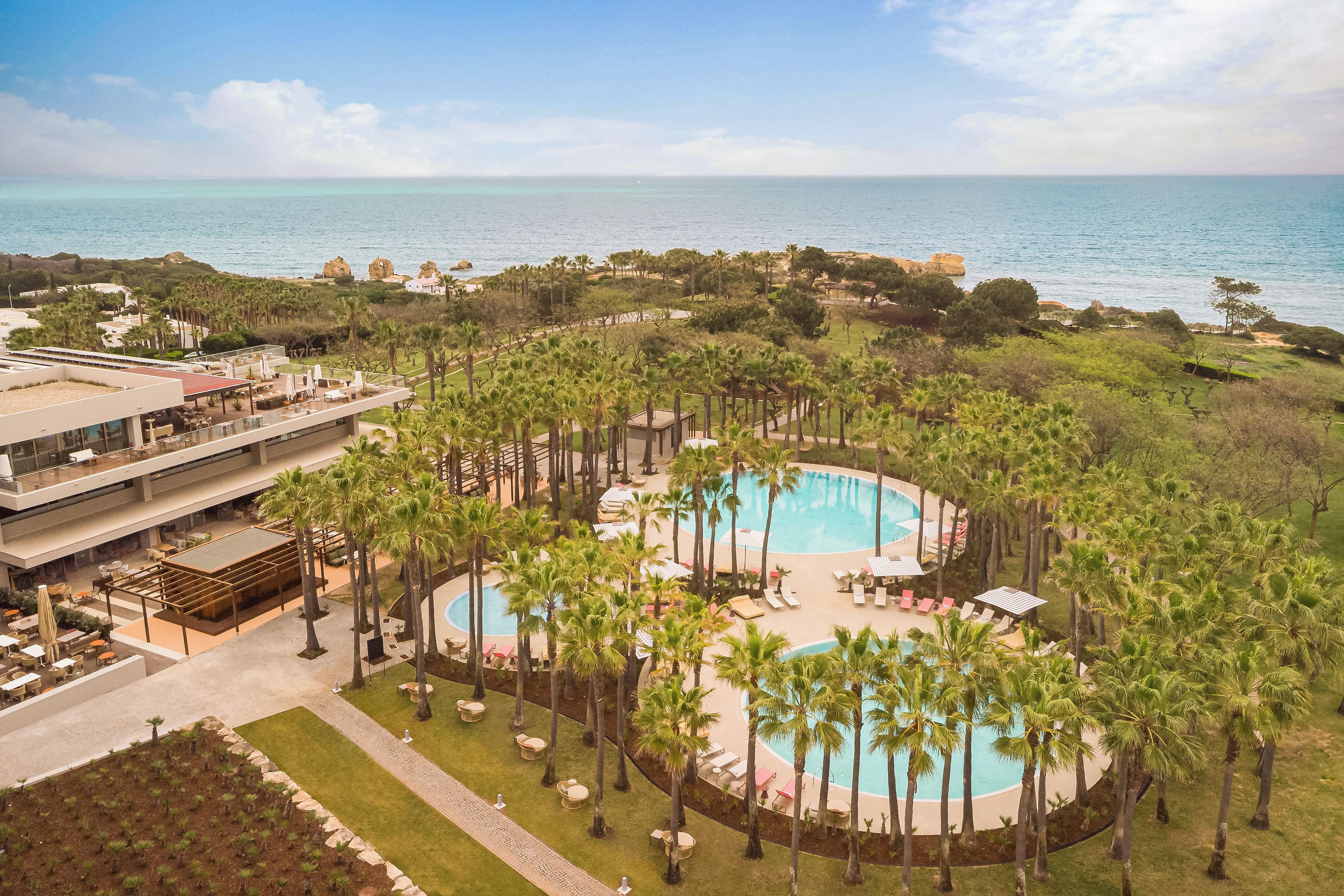 Een resort met een centraal gelegen zwembad, omringd door palmbomen, een strand en uitzicht op de zee.