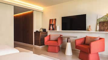 Una habitación de hotel moderna con una televisión, dos sillones rojos, una mesita redonda y un armario de madera.
