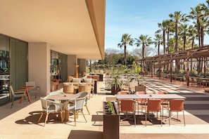 An outdoor patio with tables and chairs, surrounded by palm trees and a pergola. - Kimpton Atlantico Algarve (Albufeira)