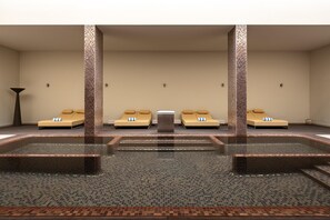 A spa area with a central hot tub, four lounge chairs, and a tiled floor. - Kimpton Atlantico Algarve (Albufeira)