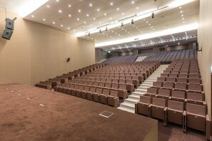 An auditorium with rows of seats, a carpeted stage area, and a ceiling with recessed lighting. - Kimpton Atlantico Algarve (Albufeira)