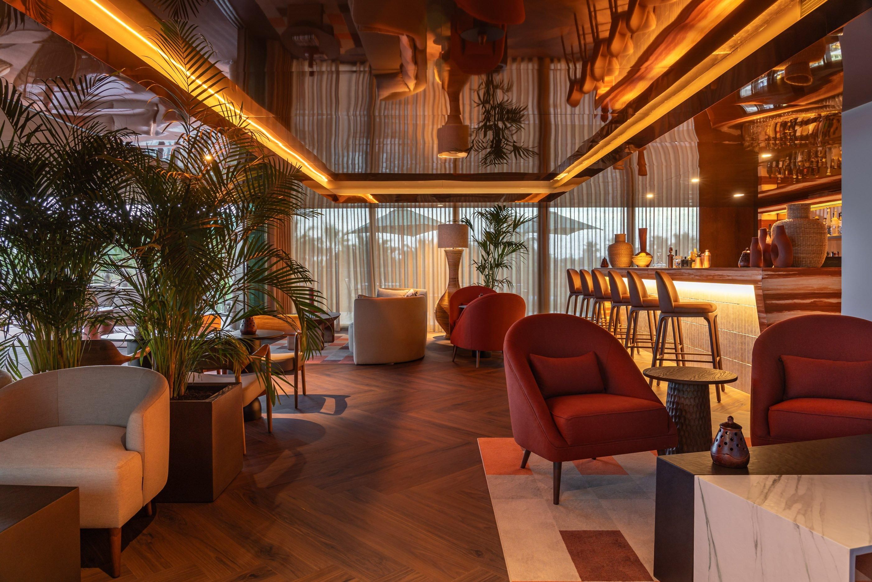 Een modern interieur met houten vloeren, rode fauteuils, een bar en grote ramen.