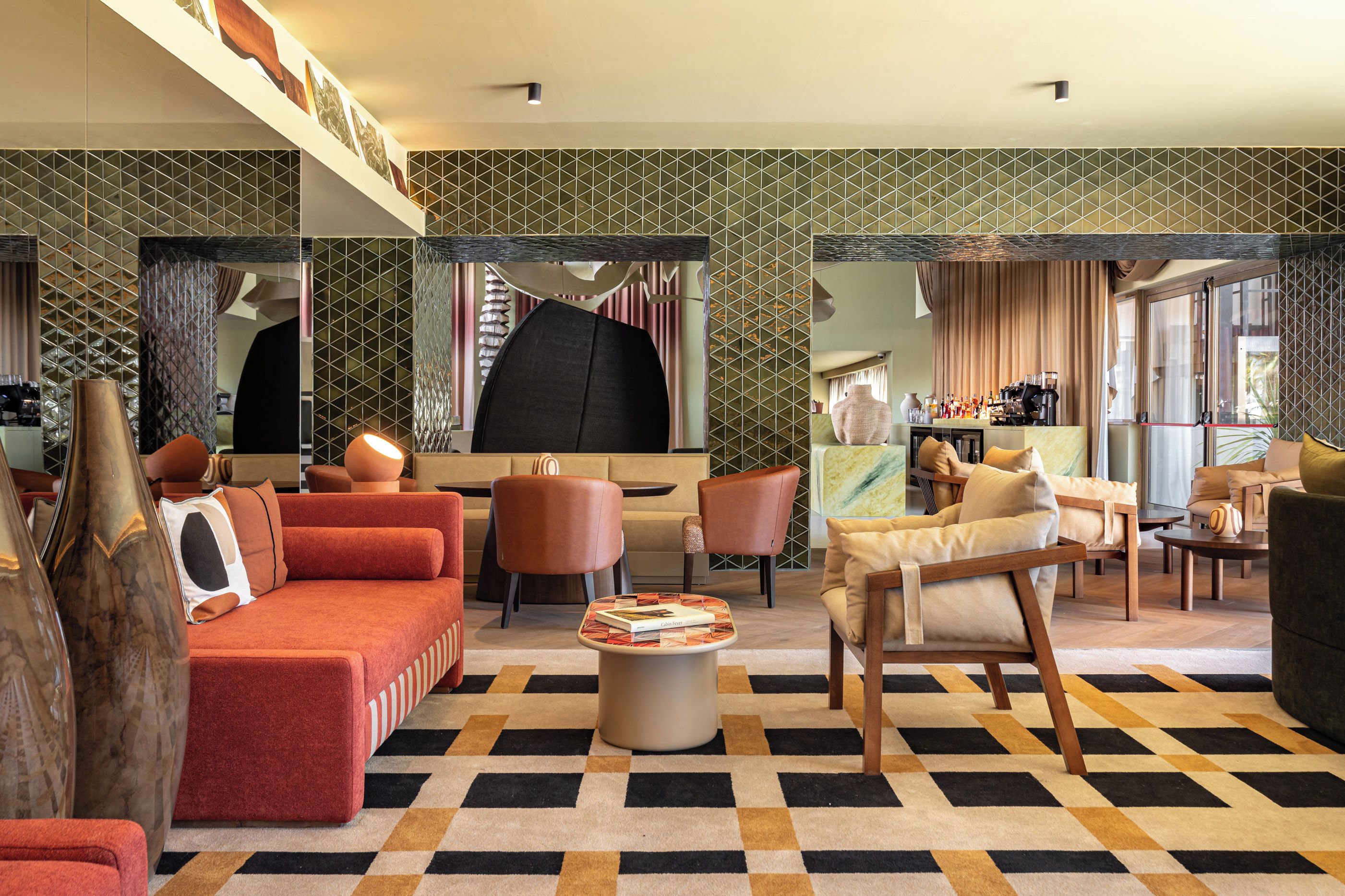 Un moderno vestíbulo de hotel con piso a cuadros, sofás rojos, sillas de madera y una barra de café.