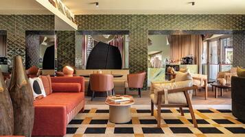 Un moderno vestíbulo de hotel con piso a cuadros, sofás rojos, sillas de madera y una barra de café.